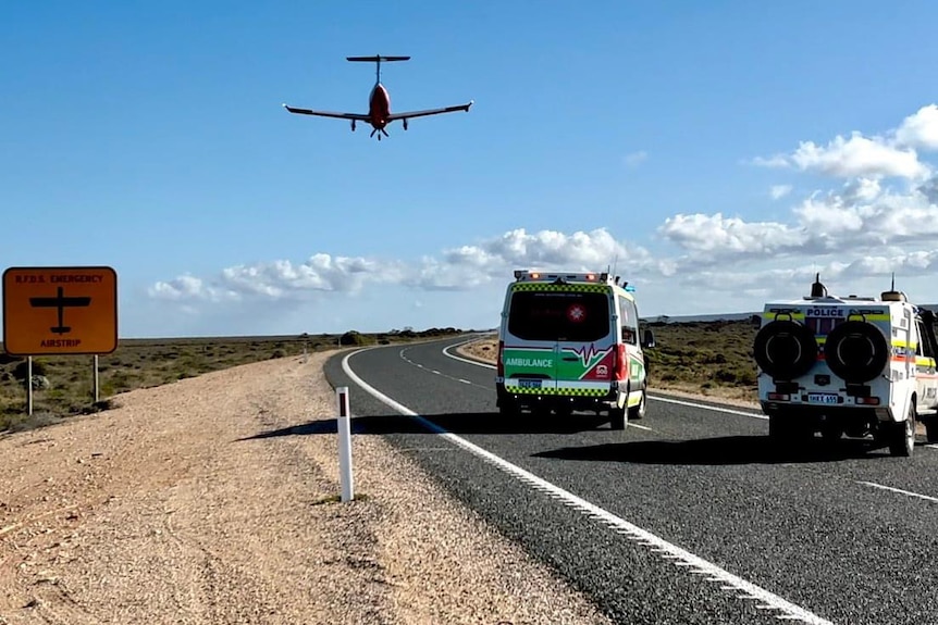 Ambulances wait as a plane lands on the road.