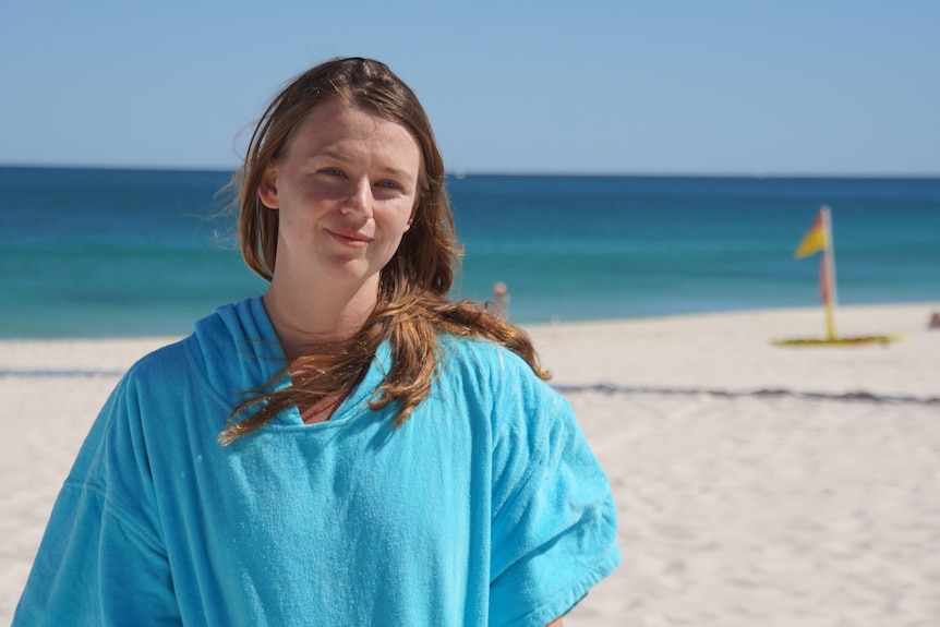 Steph smiling as she stands on Mullaloo Beach wearing a towelling pullover.