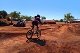 A child rides a bike on a track with jumps and berms.