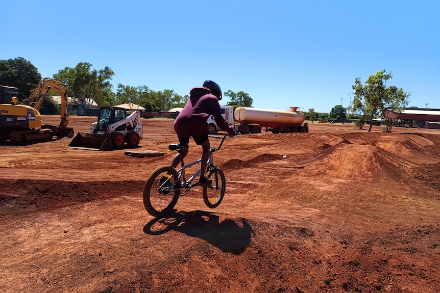 a child rides a bike on a track with jumps and berms