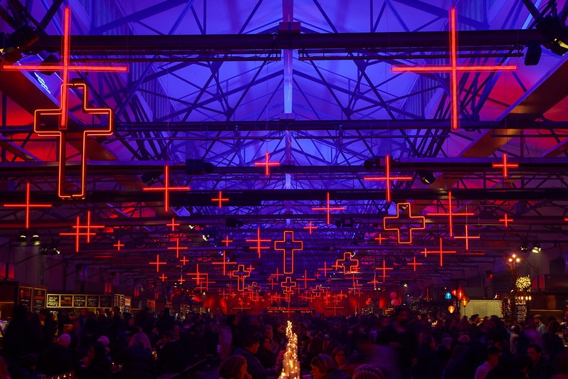 People feast in the dark indoors with lots of illuminated red crosses.