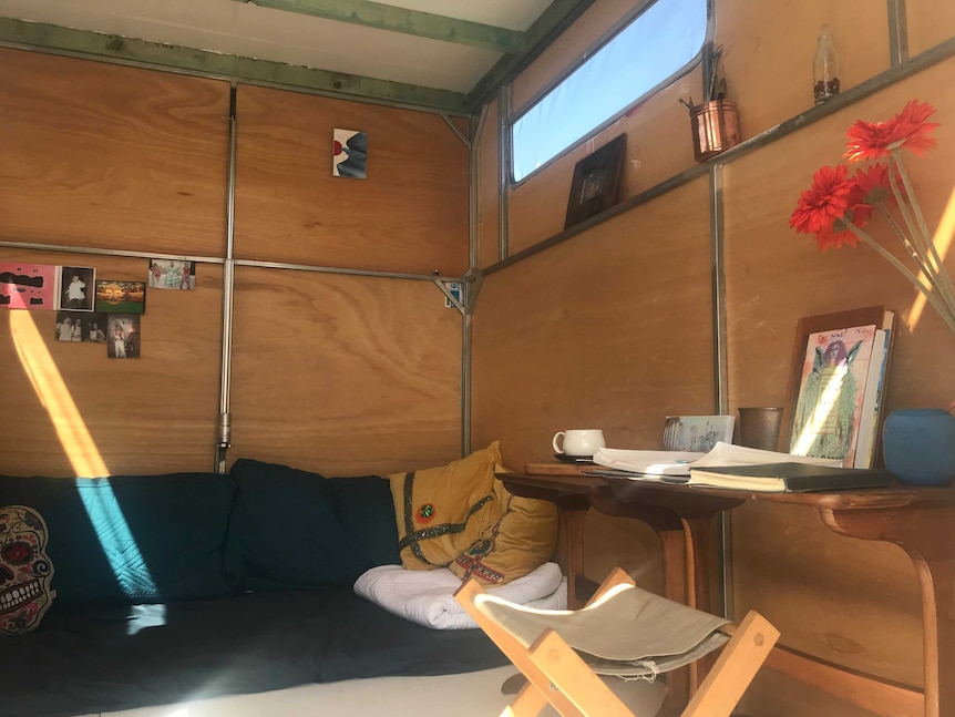 A wooden table, stool and couch surrounded by the timber walls of a tiny house.