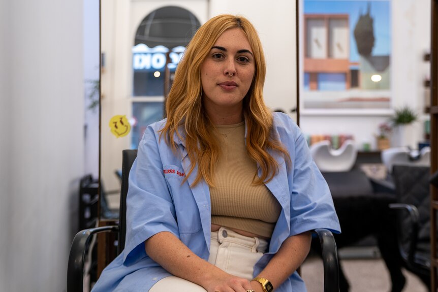 A woman with long orange hair sits in a hair salon.