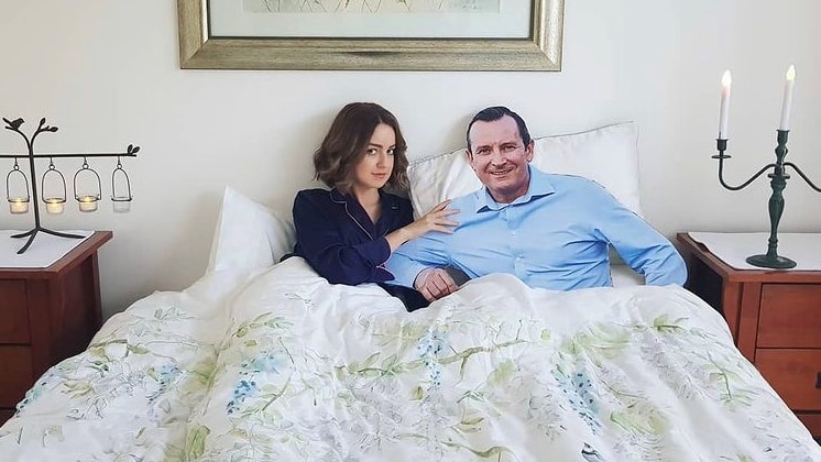 A young woman with brown hair poses in bed with a cardboard cut out of the WA Premier Mark McGowan