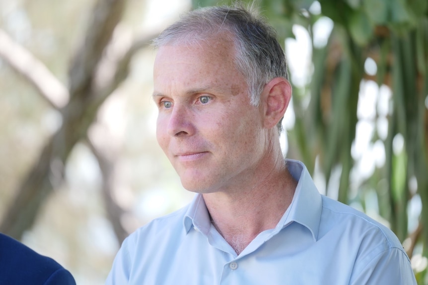 Man with white and grey hair, light blue eues and wearing a light blue collared shirt looking ahead