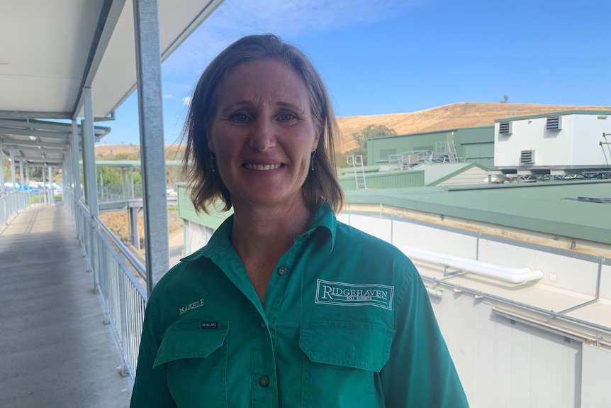 A woman in a green shirt stands in front of an abattoir. 