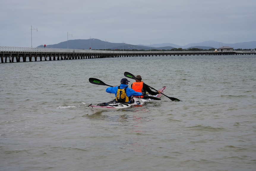 Two men paddle a kayak off into the sea.