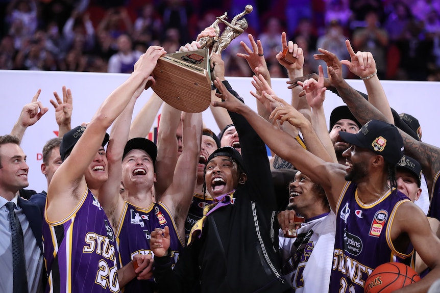 A mens professional basketball team celebrate with a trophy.