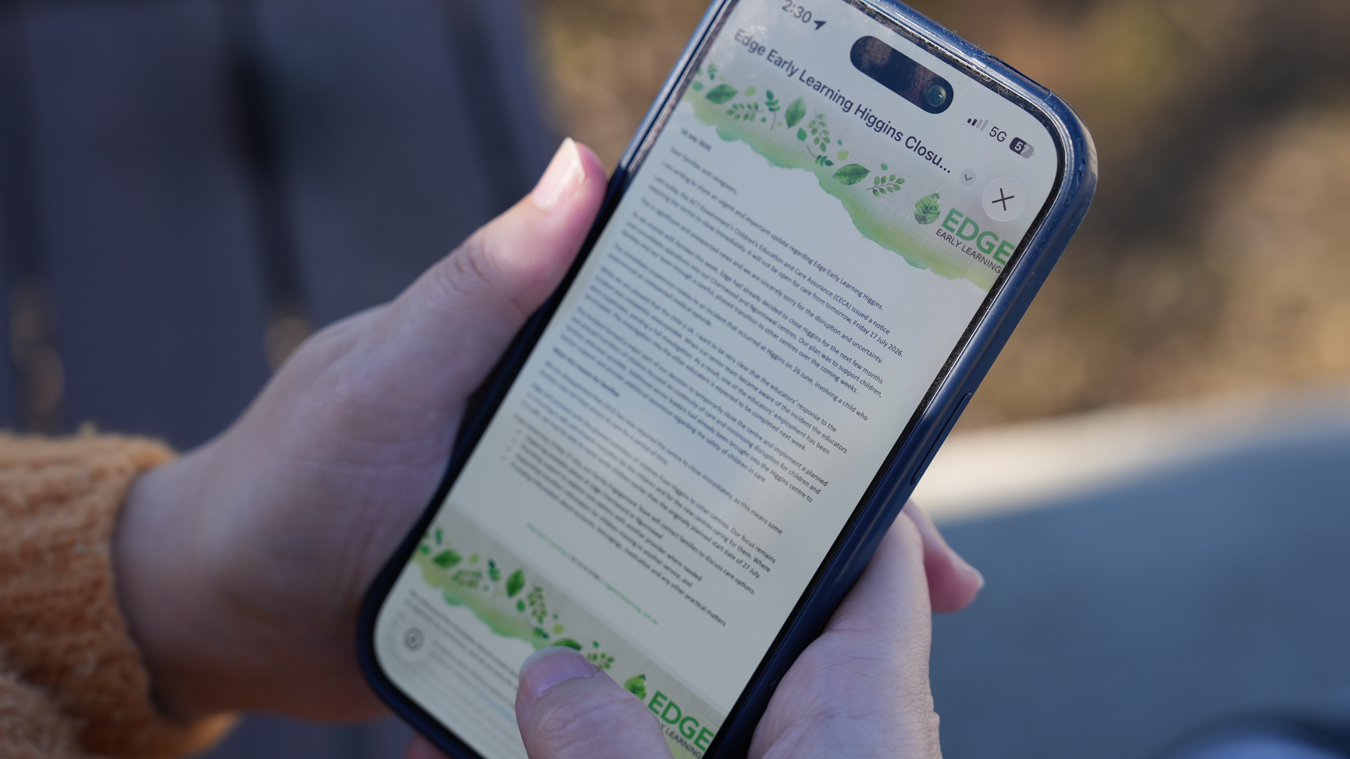 A woman holds her phone as she reads an email.