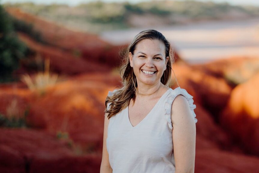 Naomi Pigrim stands in front of red rocks and beach in Broome