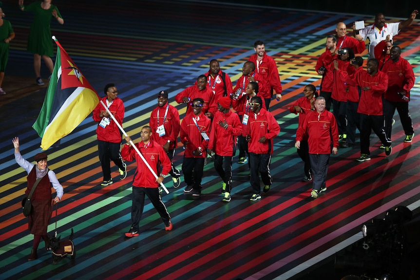 The Mozambique team, wearing red and black, march in Glasgow, with one of the athletes holding the national flag.