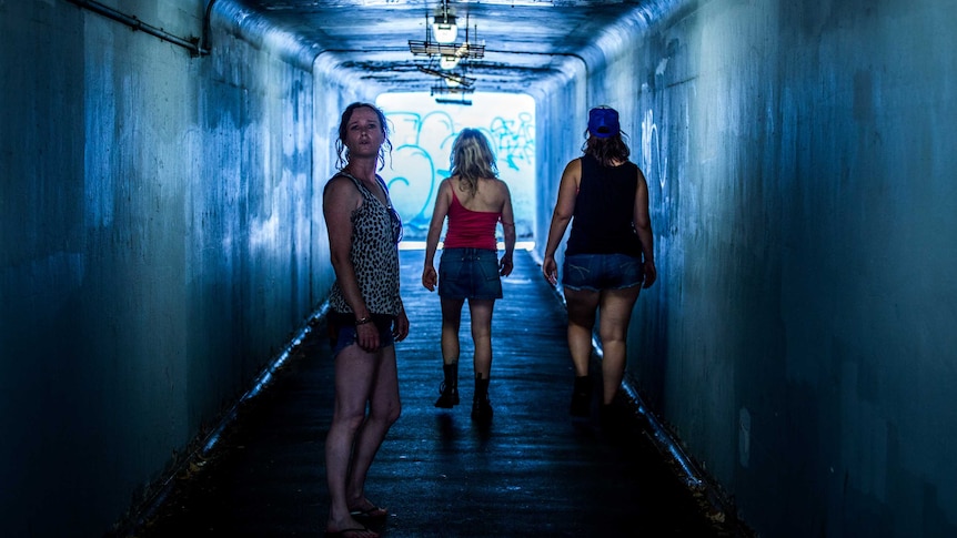 Three women walking away from the camera in a pedestrian underpass. One of the women looks behind her at the camera.
