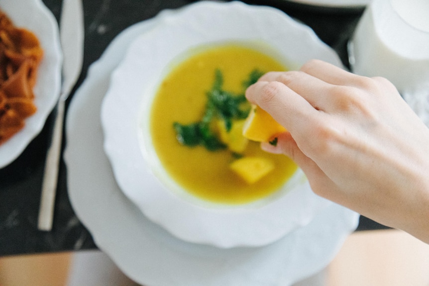Picture of hand squeezing lemon over soup.