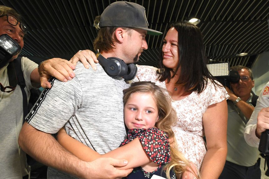 A man is embraced by his young daughter and wife.
