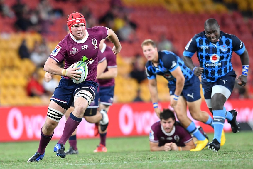 A rugby player wearing head gear looks to step inside as he runs with ball in a Super Rugby game.