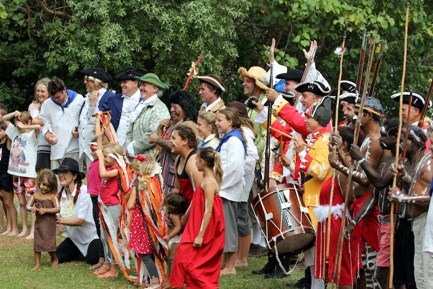 Group of people in costume including 18th Century British marines and Aboriginal people with body paint and spears.