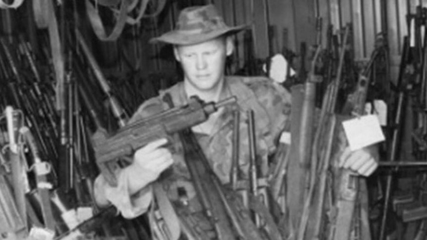 Black and white photo of Australian soldier Michael Handley surrounded by guns during his peacekeeping operations in Somalia.