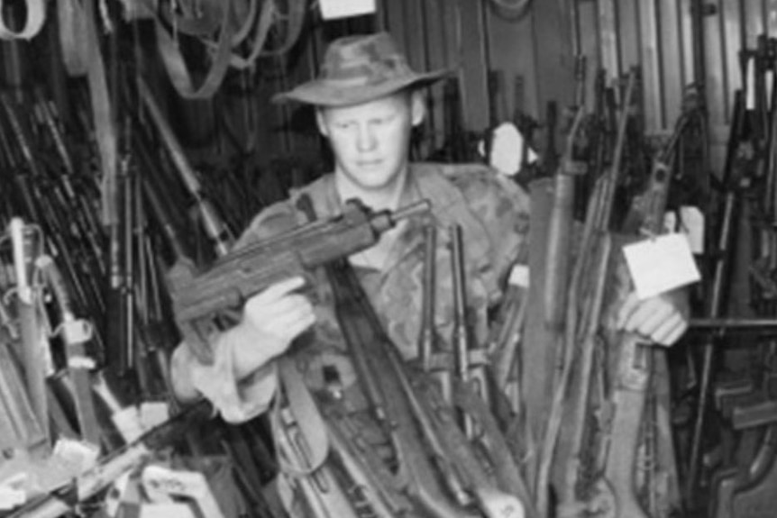 Black and white photo of Australian soldier Michael Handley surrounded by guns during his peacekeeping operations in Somalia.