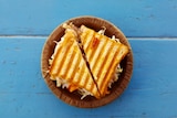 A toasted sandwich on a paper plate sitting on a blue table