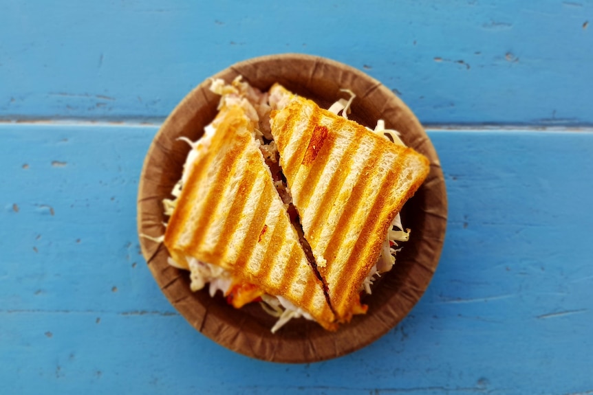 A toasted sandwich on a paper plate sitting on a blue table