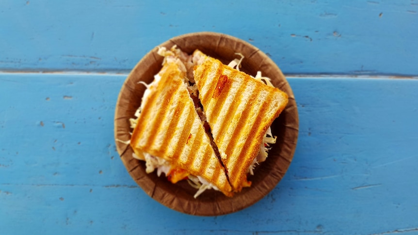 A toasted sandwich on a paper plate sitting on a blue table