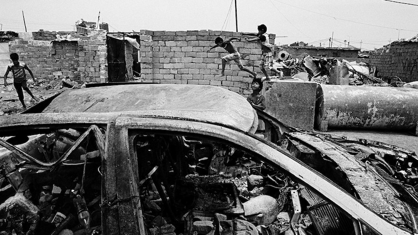 Iraq gypsy children play in the rubble of buildings and a destroyed car.