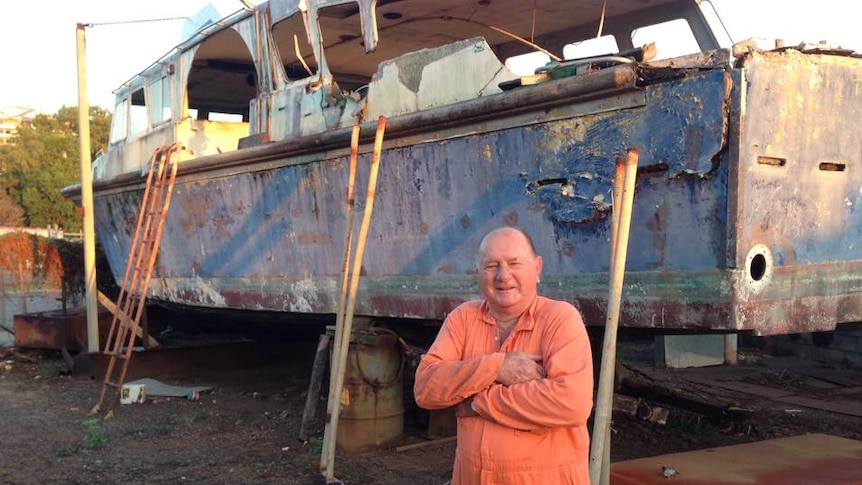 A man standing in front of a very old and knocked about ship.