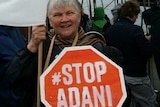 A woman smiles as she holds a Stop Adani sign