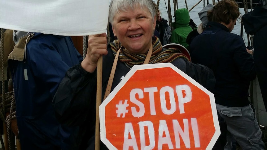 A woman smiles as she holds a Stop Adani sign