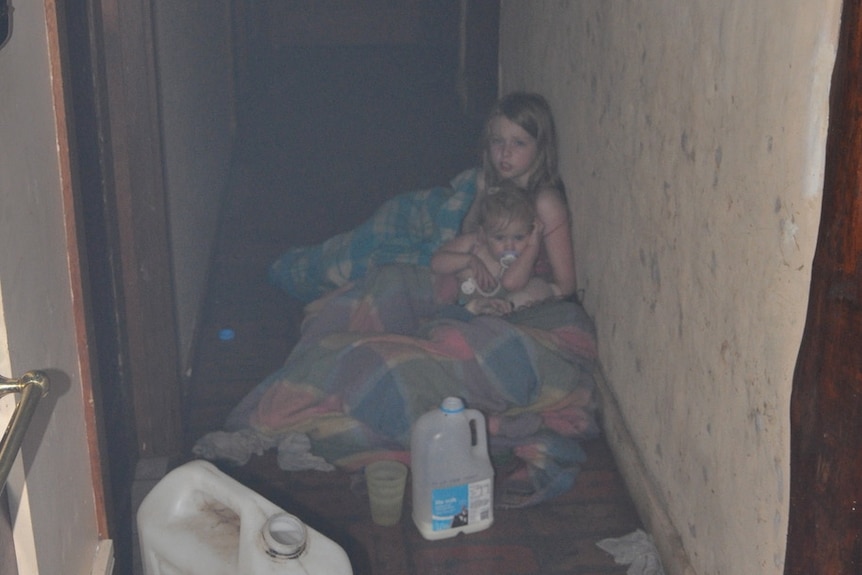 A grainy photo of a young girl and baby, covered in woolen blankets in a smoky hallway.