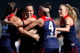 Five Melbourne AFLW players embrace as they celebrate a goal against the Kangaroos.