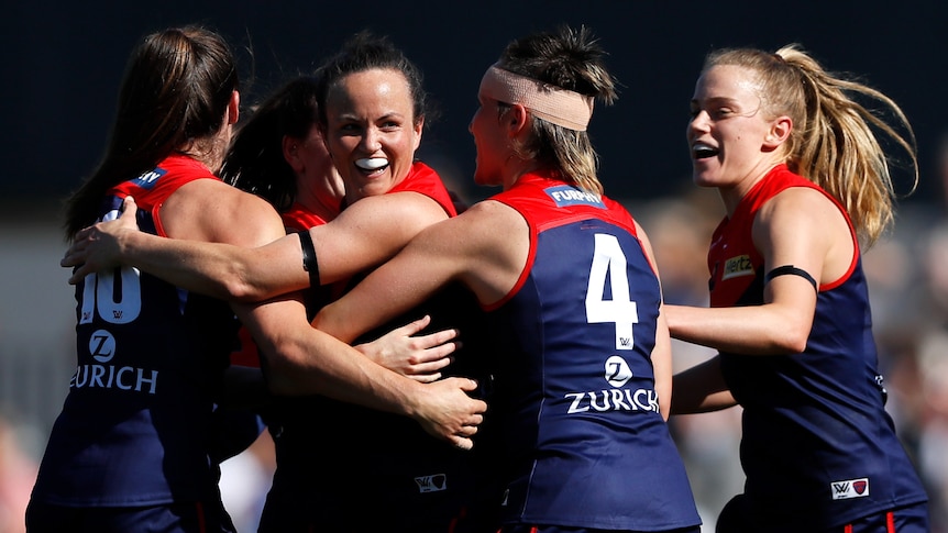 Five Melbourne AFLW players embrace as they celebrate a goal against the Kangaroos.