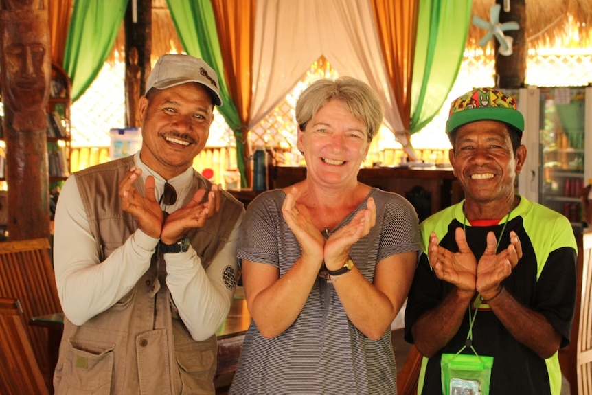 Karen Edyvane flanked by two men make a gesture with their hands. 