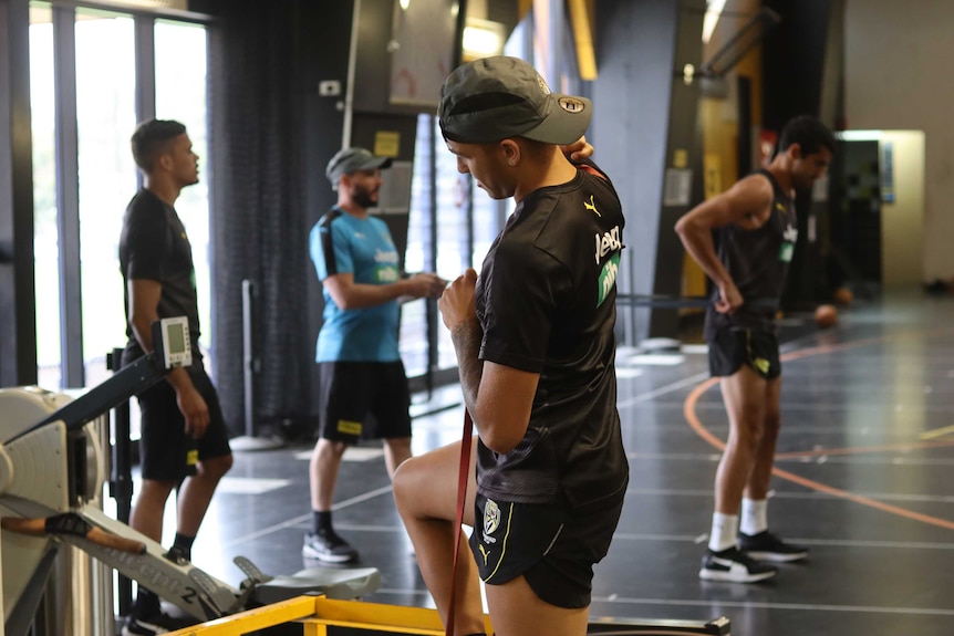 Three men train in a gym undertaking various exercises