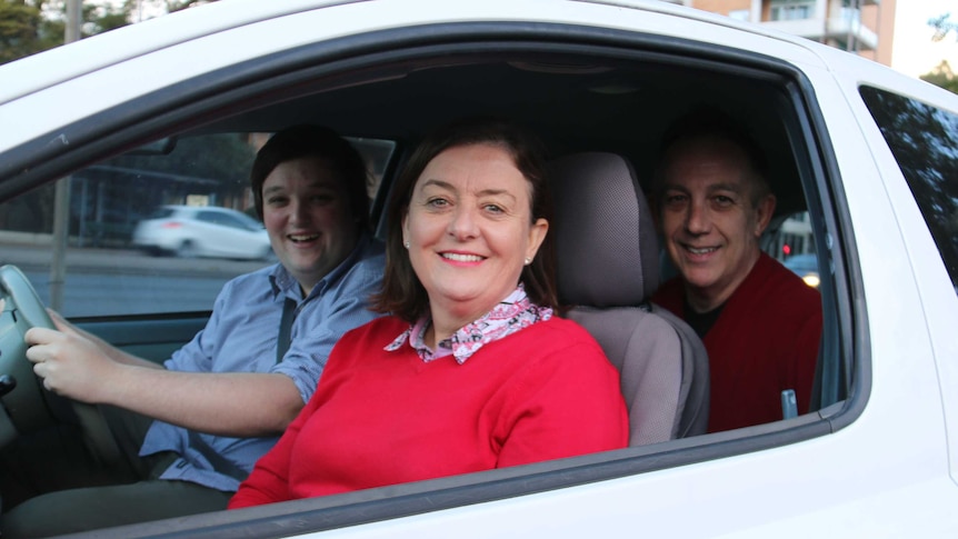 Two parents sit in passenger seats with their son driving