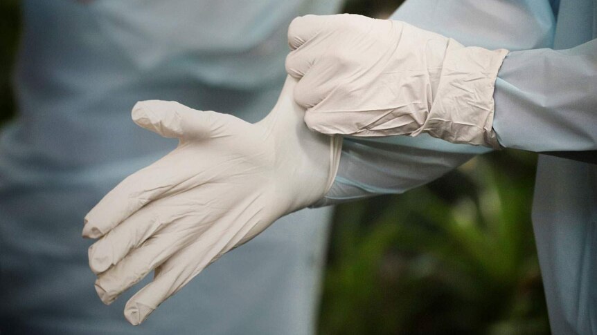 Two hands connected to a person in full protective gear adjust white surgical gloves.