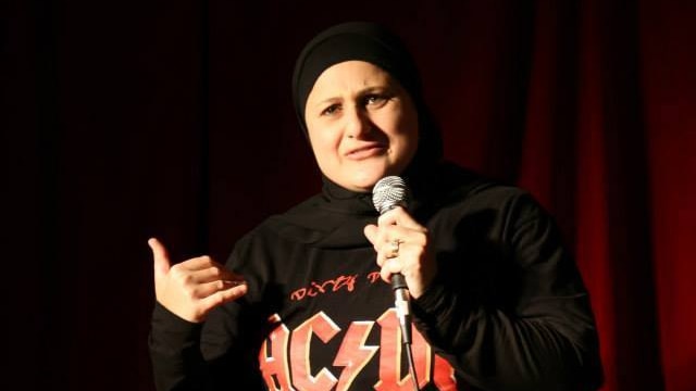 Frida Deguise holds a microphone on stage while wearing an AC/DC shirt