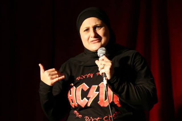 Frida Deguise holds a microphone on stage while wearing an AC/DC shirt