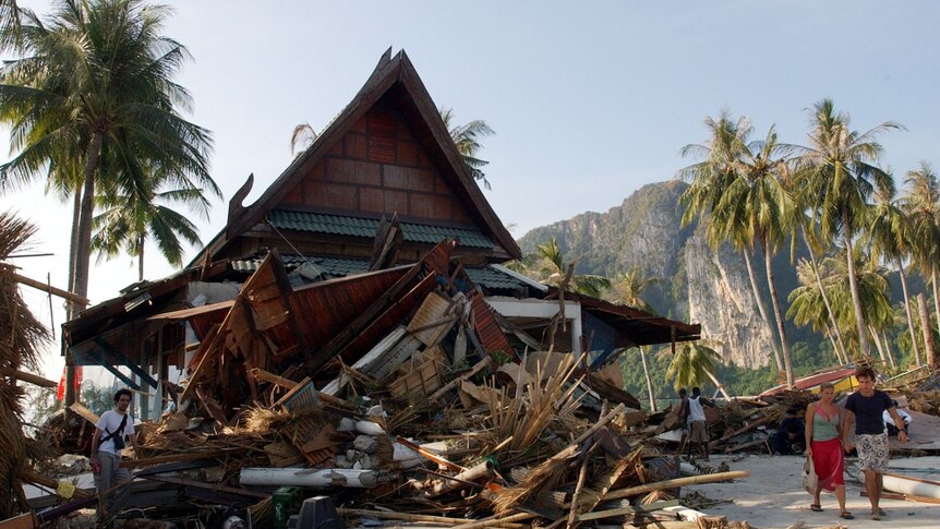 A pile of debris sits out the front of a holiday villa. A Thai mountain and palm trees are in the background