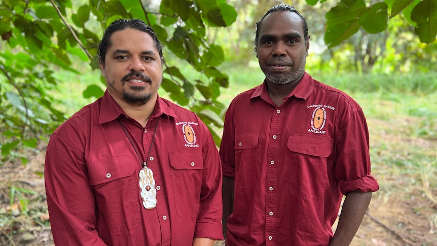 Two men wearing burgundy work shirts standing in a forested area