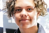 A close-up shot of a young man with wavy brown hair.