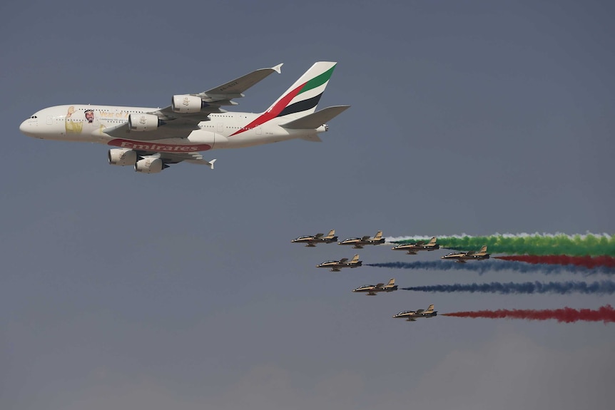 An Emirates A380 flies ahead of an air force aerobatic display team.