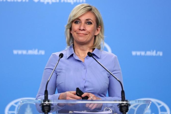 Blonde woman in blue collared shirt stands at microphone