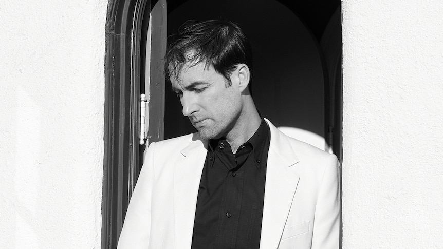 Black and white photo of Andrew Bird wearing a white suit, staring downwards