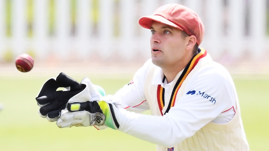 A South Australian Sheffield Shield wicketkeeper attempts to catch a ball while wearing gloves.