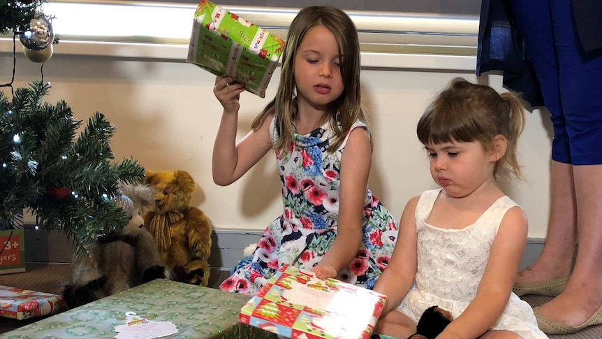 Chloe Fowler, 7, and Chelsea Fowler, 3, look at presents under a christmas tree.