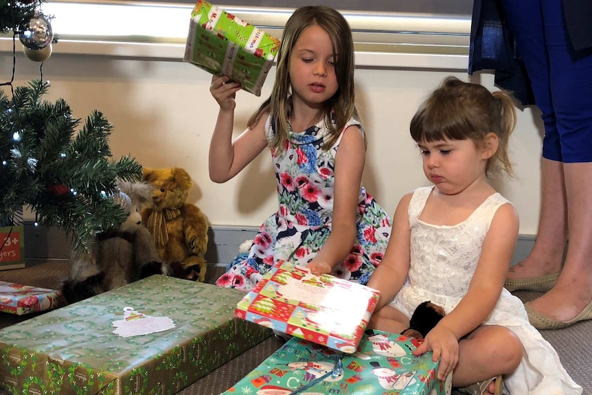 Chloe Fowler, 7, and Chelsea Fowler, 3, look at presents under a christmas tree.