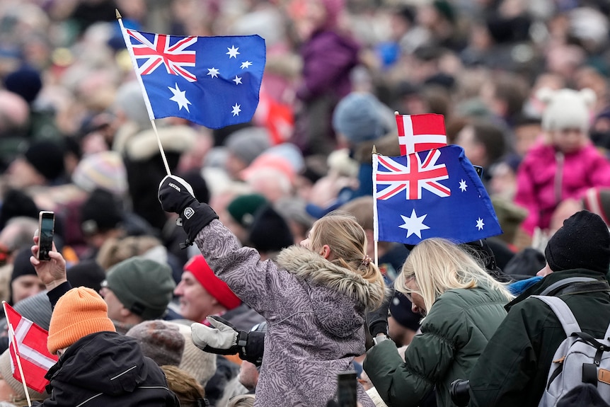 A girl in a crowd waves two Australian flags