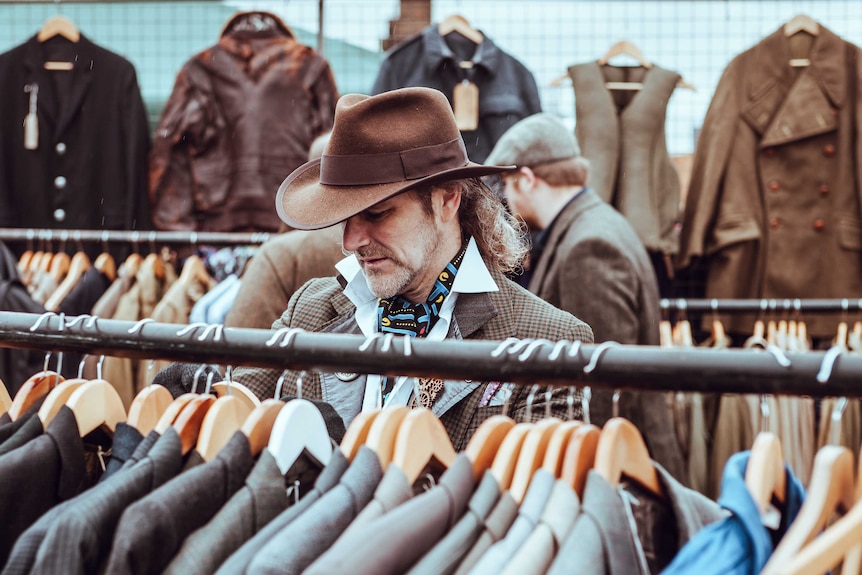 A man in a hat browsing a clothes rack