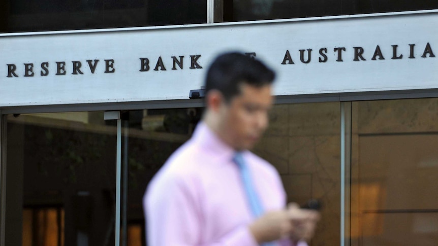 A man in a pink business shirt walks past the Reserve Bank building in Sydney. 